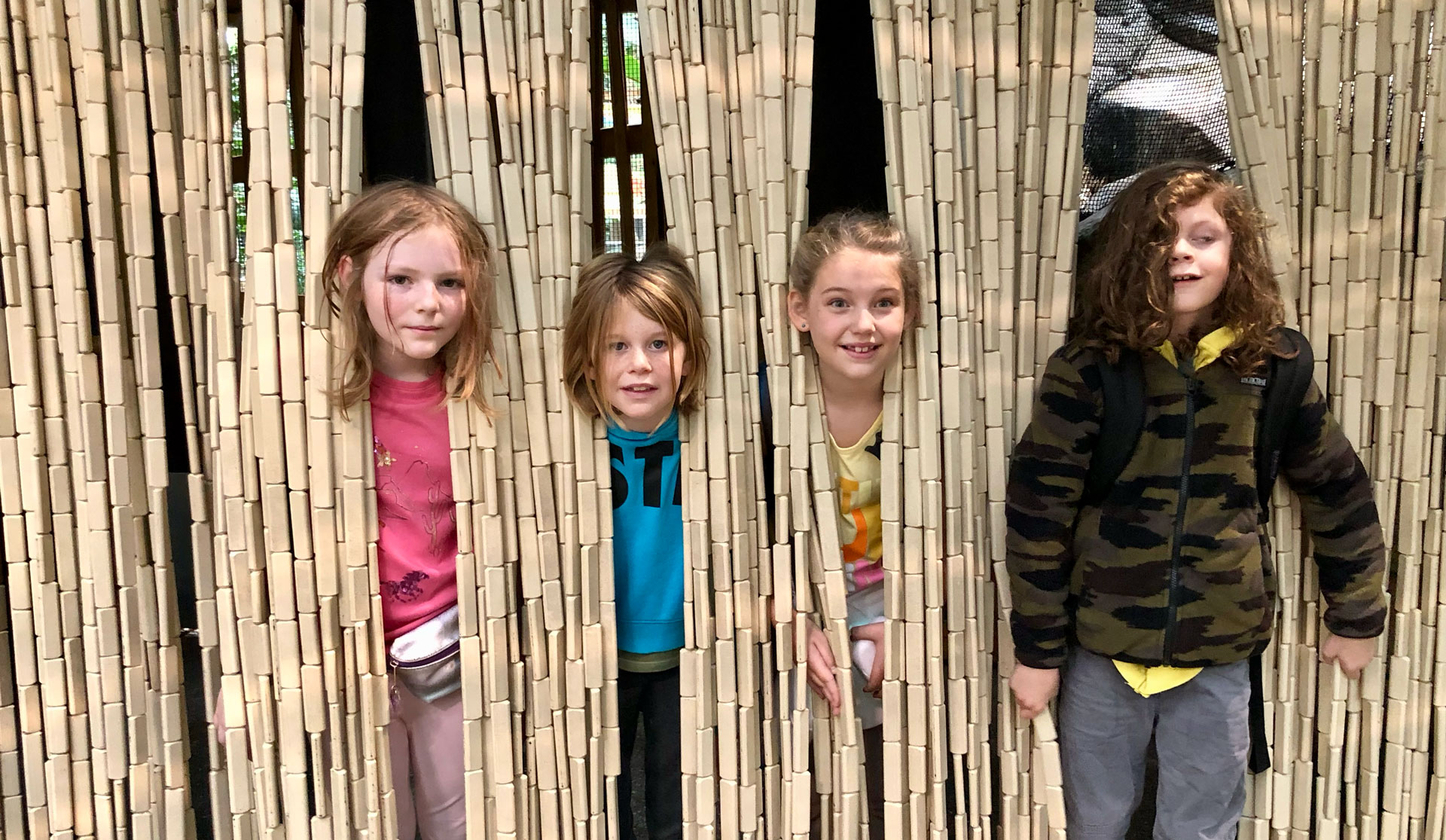 4 students sticking heads out from bamboo fence